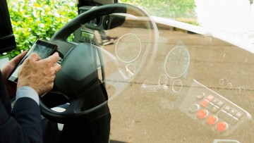 Busfahrer mit Smartphone in der Hand hinterm Buslenkrad