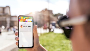 Ein junger Mann mit Deutschland-Ticket auf seinem Smartphone in städtischer Umgebung