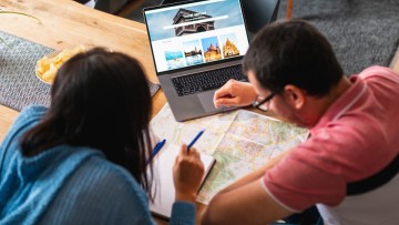 Reiseplanung: Ein Paar, das gerade eine Reise plant mit Landkarte und Laptop